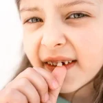 Child touching loose baby tooth while checking it