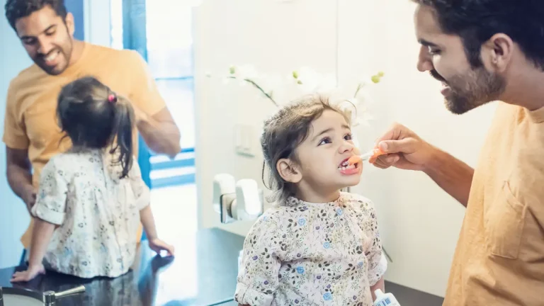 Father helping young child brush teeth before dental visit