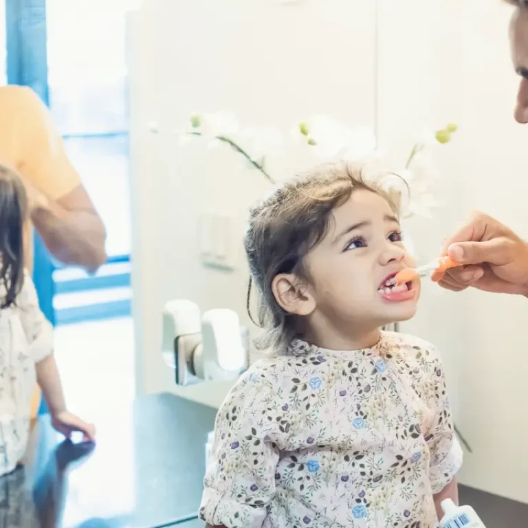 Father helping young child brush teeth before dental visit